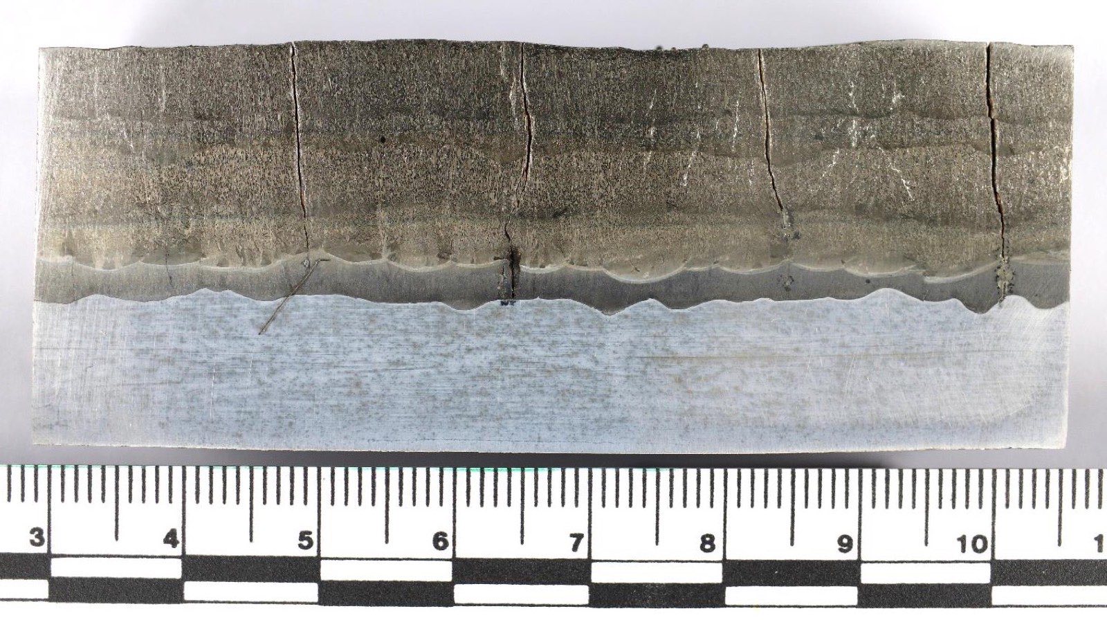 Macro cross-section of CCO plate showing overlay layers and relief cracks arresting at the fusion line